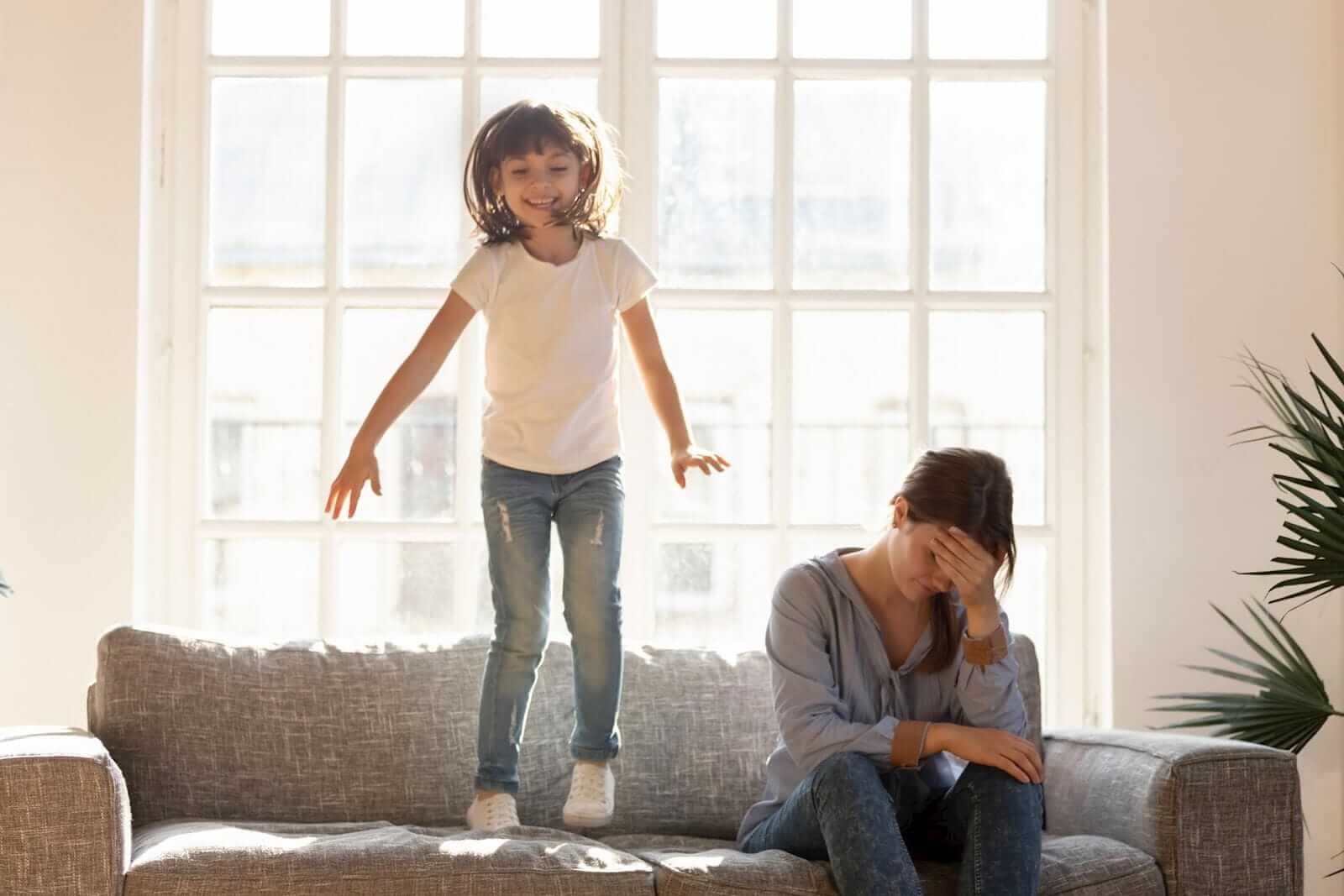child jumping on the couch while mom sits with head in hands