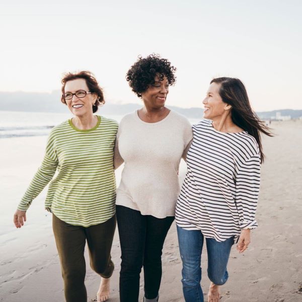 three women walking arm in arm on beach