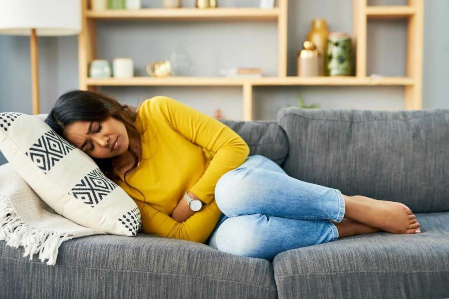 woman lying on couch holding stomach in pain