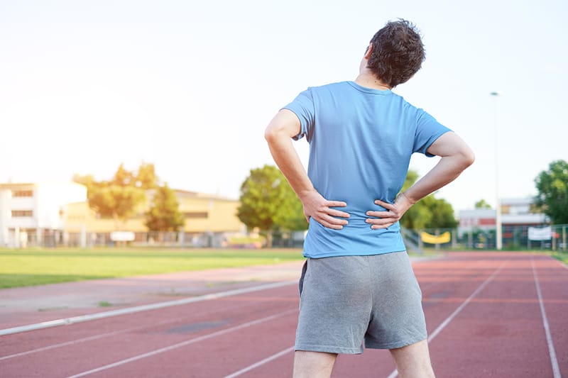 man running on track clutching lower back in pain