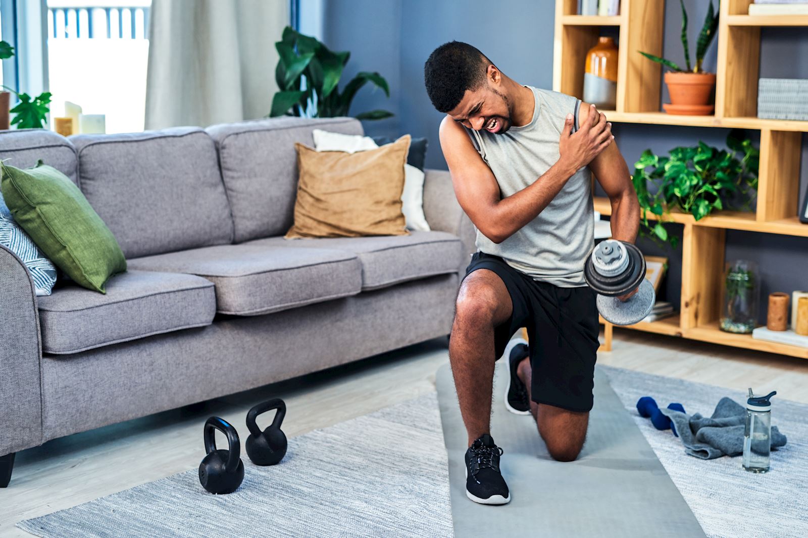 man working out in living room grabbing shoulder in pain