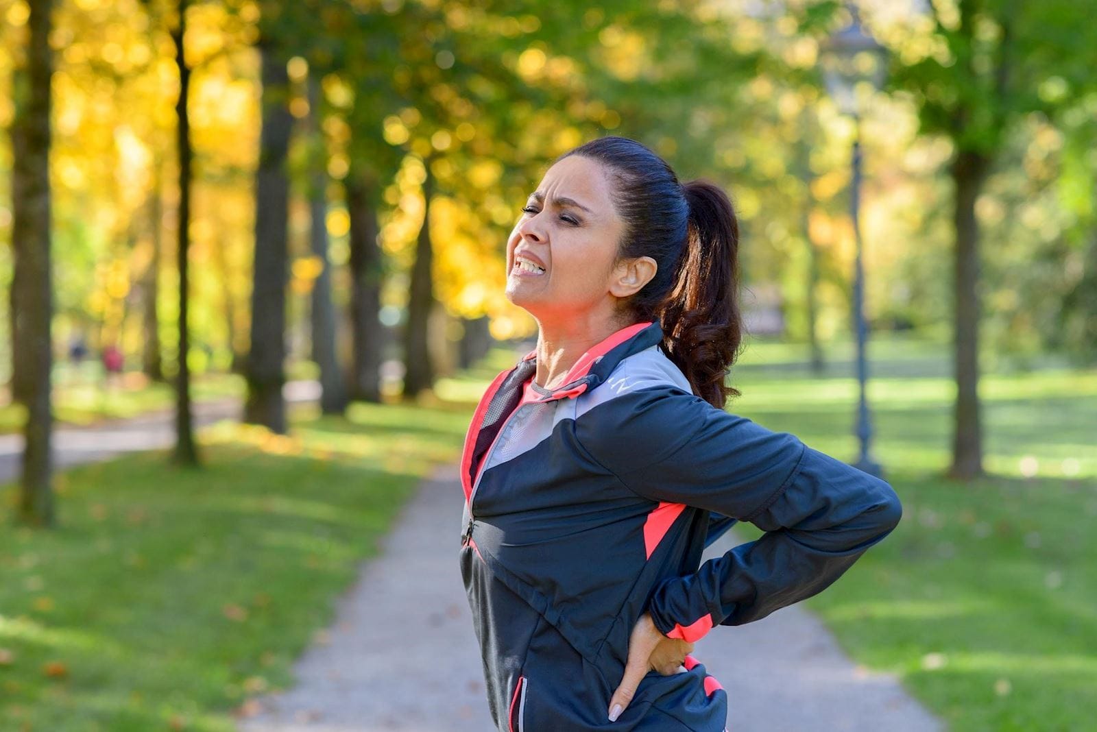 woman running on a trail holding her back in pain
