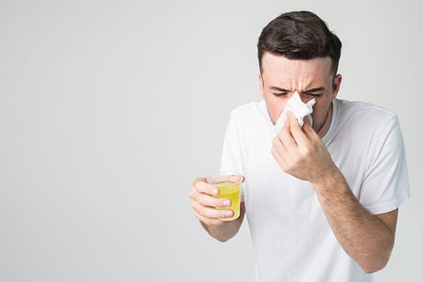 man with glass of orange juice blowing nose