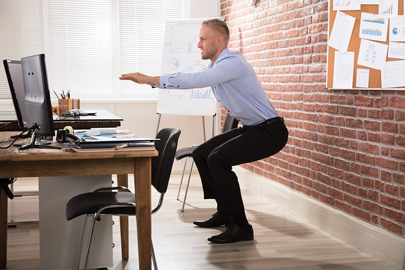 man doing squats at his desk