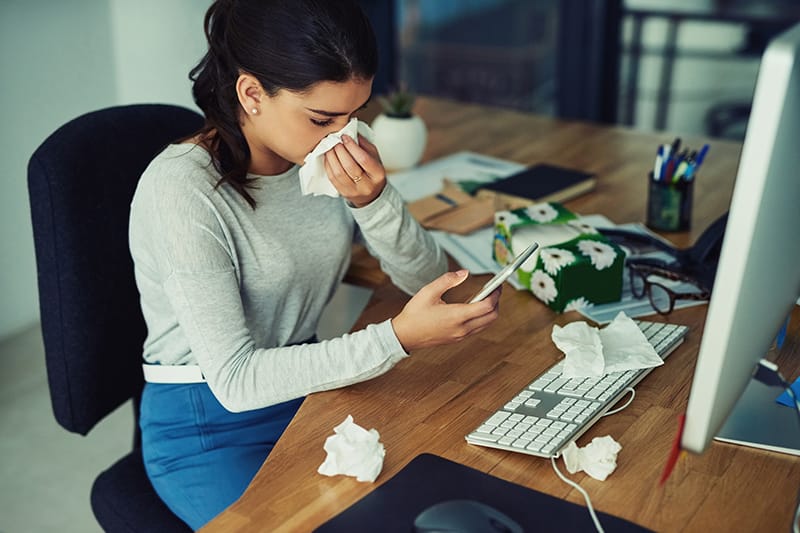 woman looking at her phone while holding a tissue to her nose