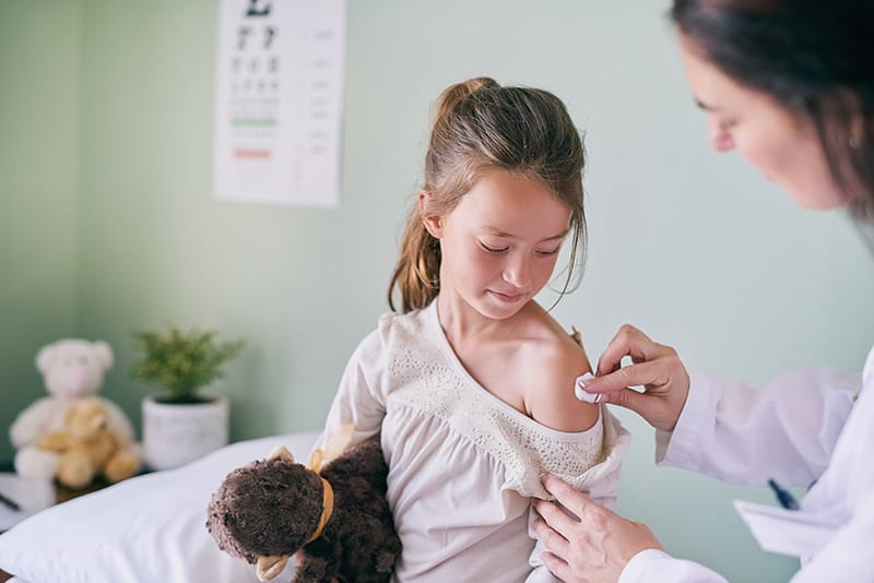 Doctor cleaning arm of young girl before giving a vaccine