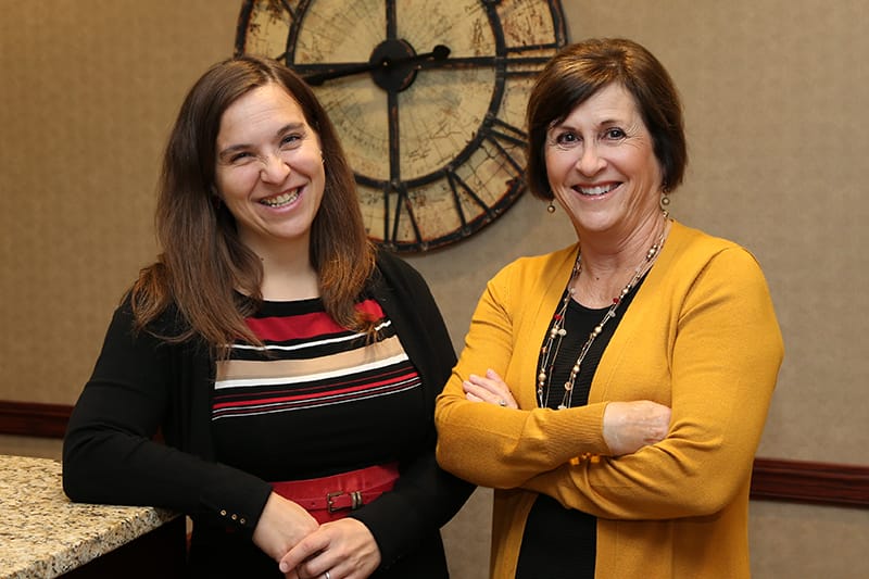 two women stand by eachother, smiling