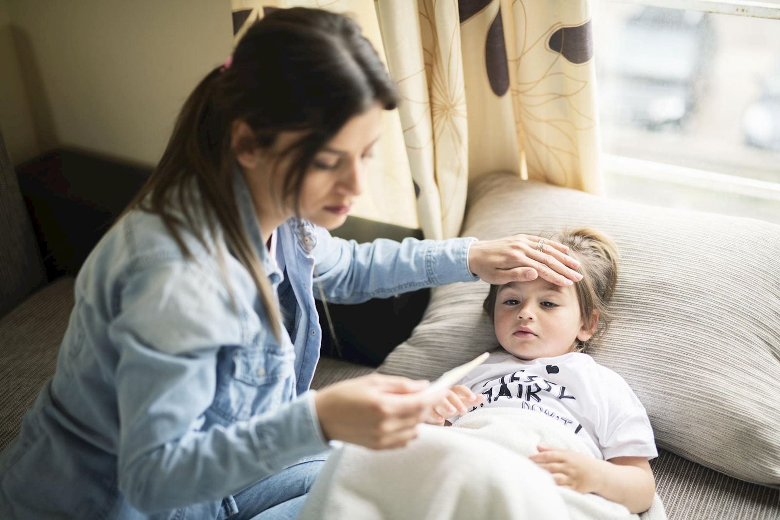 mother checks daughters temperature with thermometer