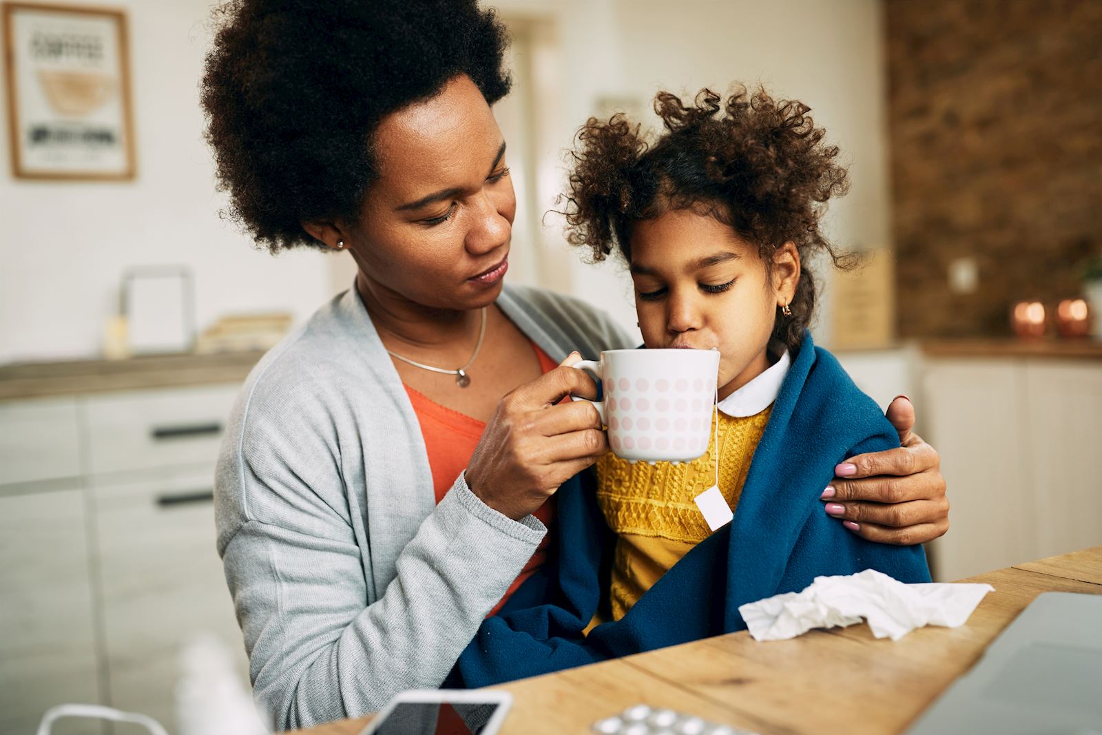 woman helps sick daughter drink tea