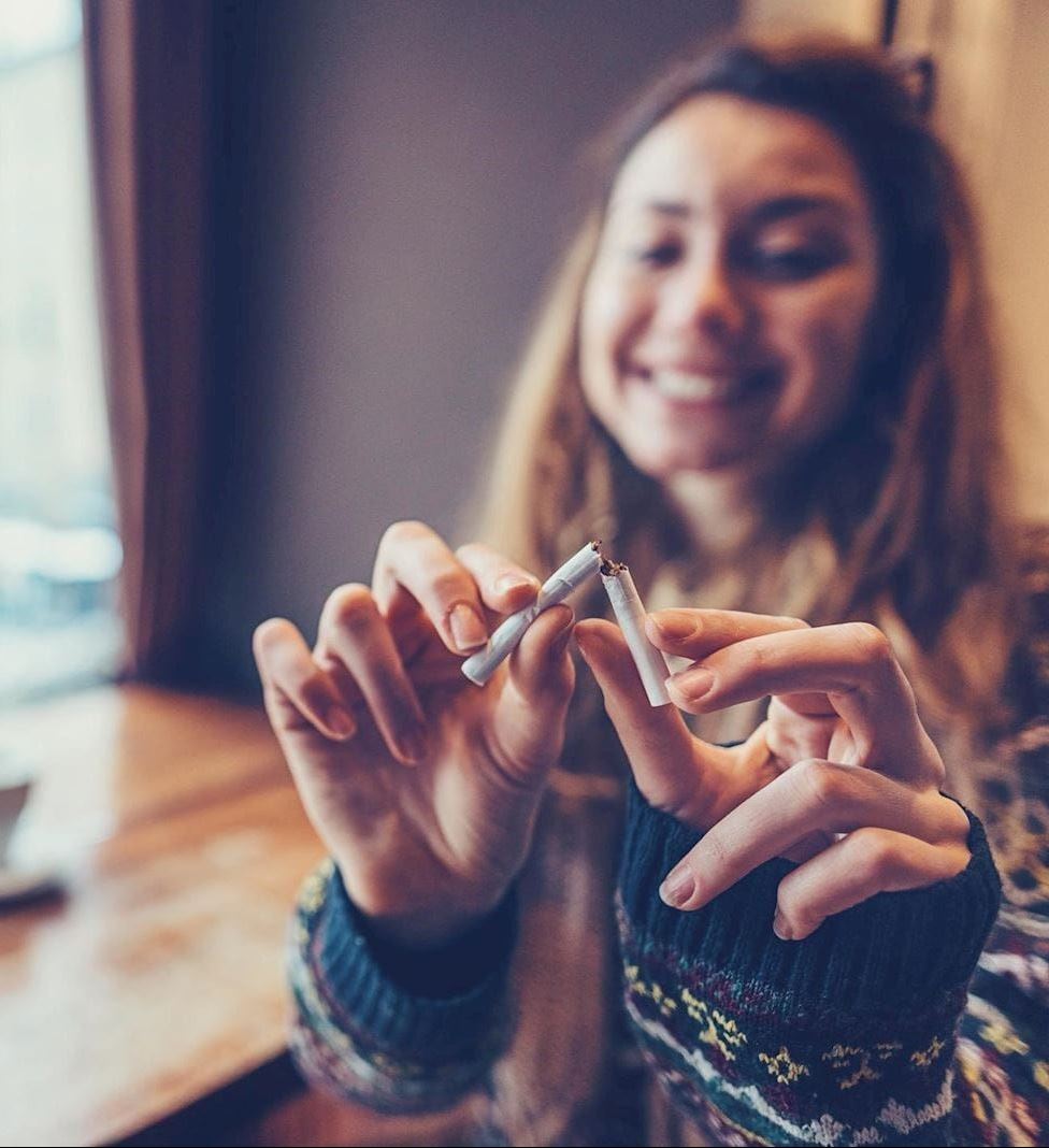 smiling woman breaks cigarette in half