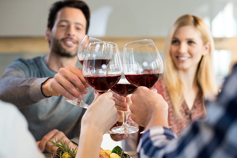 group of people doing cheers with glasses of red wine