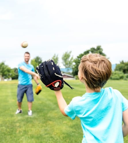 dad throwing baseball to young son wearing baseball glove