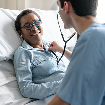 Patient laying in hospital bed with doctor checking their heart