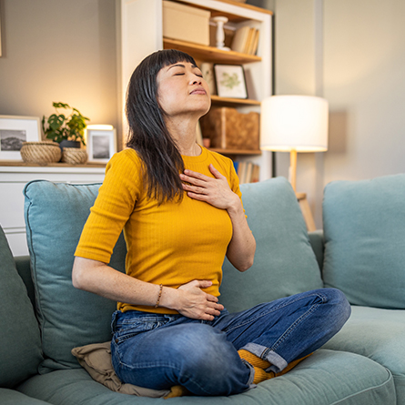 Woman sitting on couch with one hand on chest and one on stomach