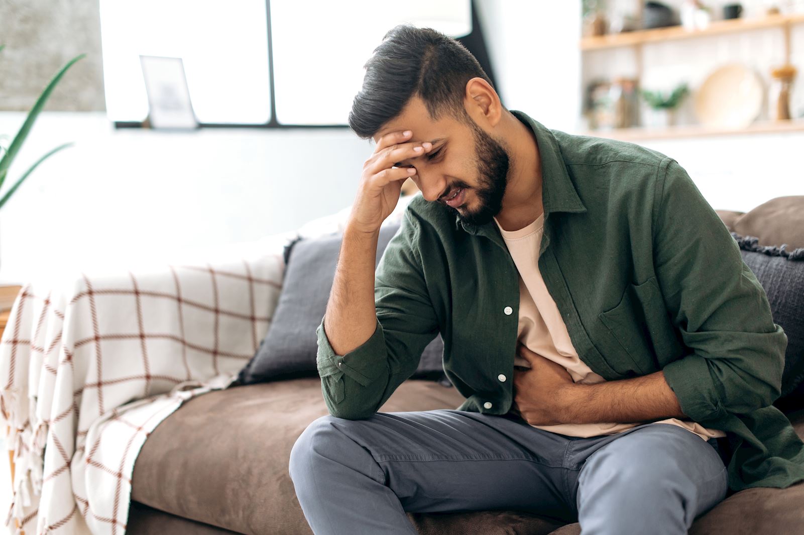 Man with head in hand clutching stomach in pain