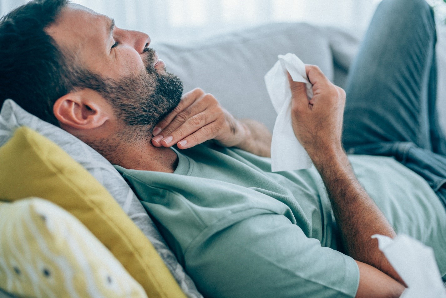 man laying on couch holding his sore throat
